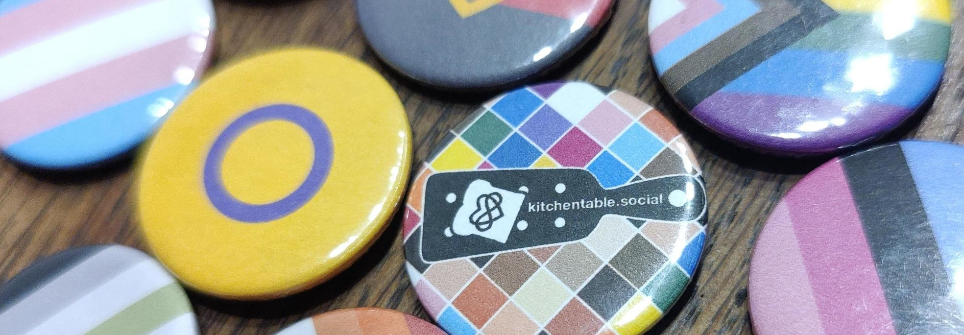 a collection of pride buttons, one of them with the Kitchen Table symbol